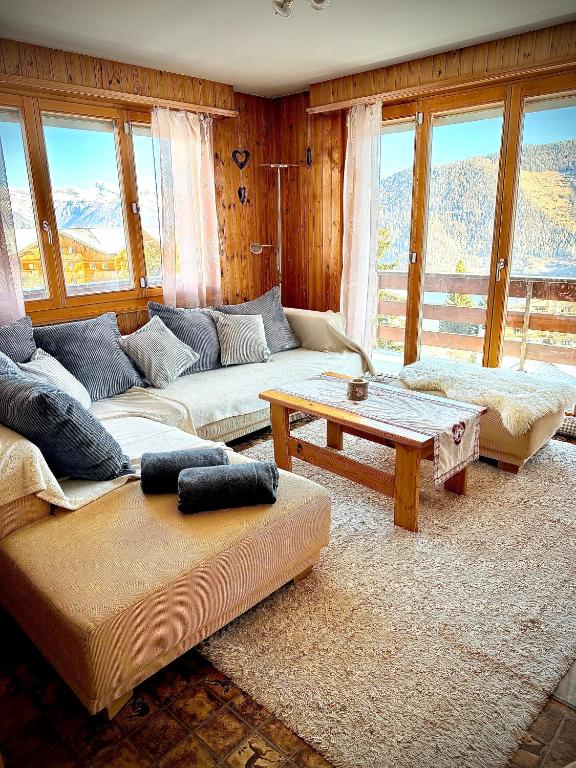 a living room with couches and a table and windows at Appartement au pied des télécabines in La Tzoumaz