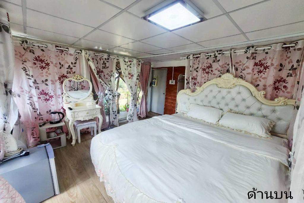 a bedroom with a large white bed with pink curtains at Merlin Hut & Farm in Kanchanaburi City