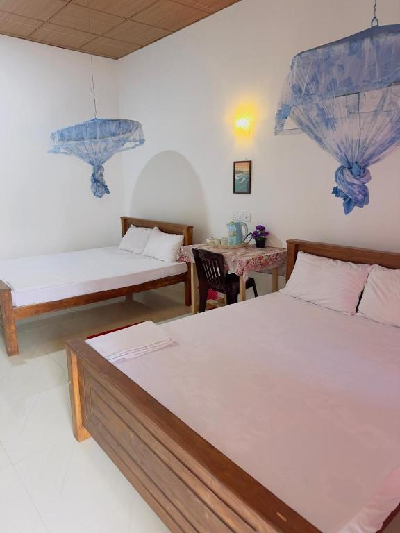 a bedroom with two beds and a table in it at Wilpattu Lakwin Guest in Pahala Maragahawewa