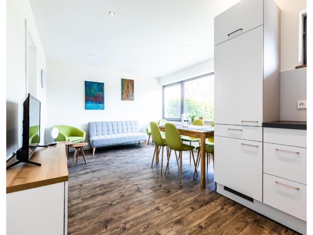 a kitchen and dining room with white cabinets and green chairs at Bungalow im Campingpark in Waxweiler
