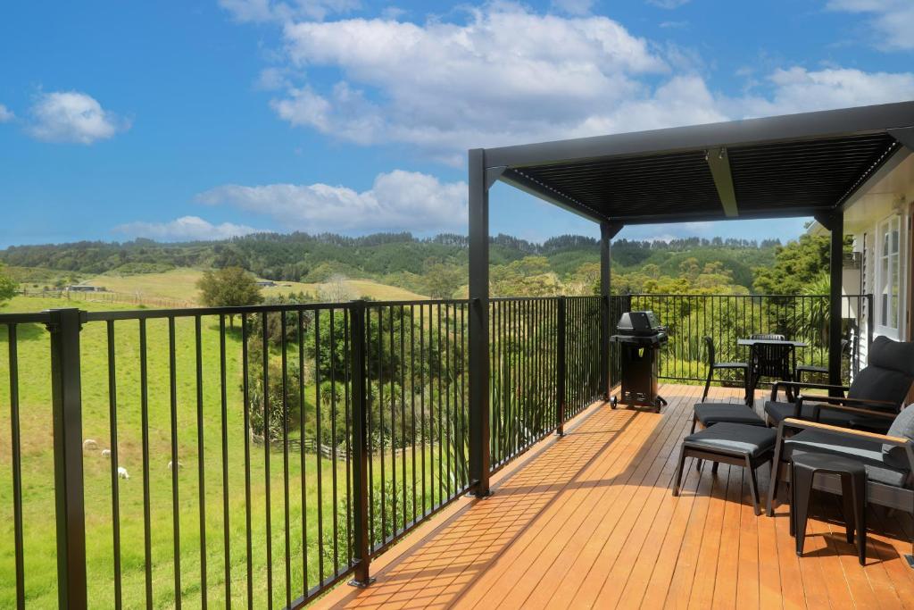 a wooden deck with chairs and a grill on aestead at Glenmohr Cottage in Waipu