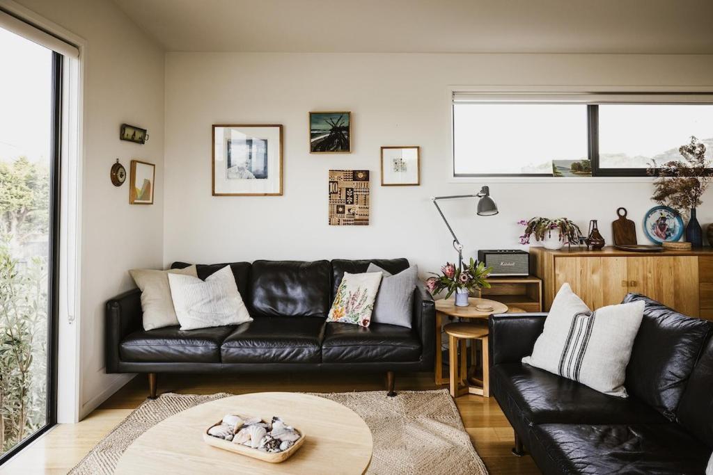 a living room with a black leather couch and a table at Moonbird Beach Shack ~ Ocean Escape in Beaumaris Tasmania