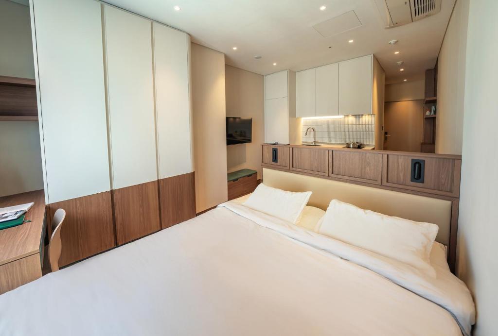 a bedroom with a large white bed and a kitchen at Weave Suites - Sunyu Parkside in Seoul