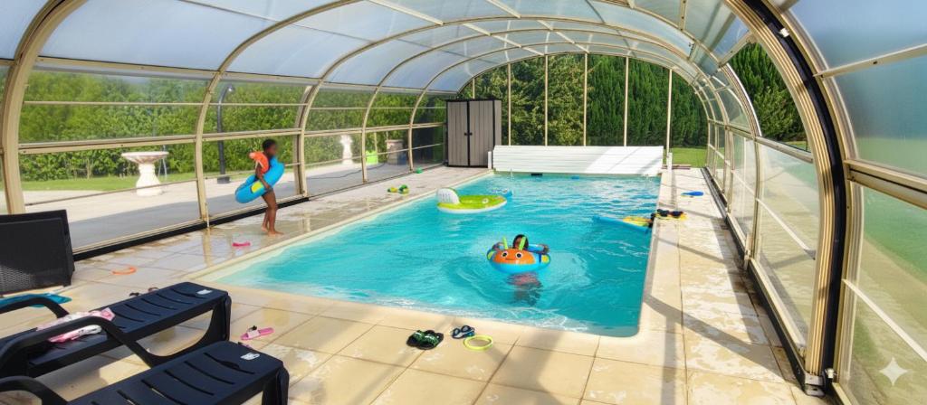 a woman in a swimming pool in a dome with a person in the water at Villa au calme, piscine couverte chauffée 365j in Thiberville