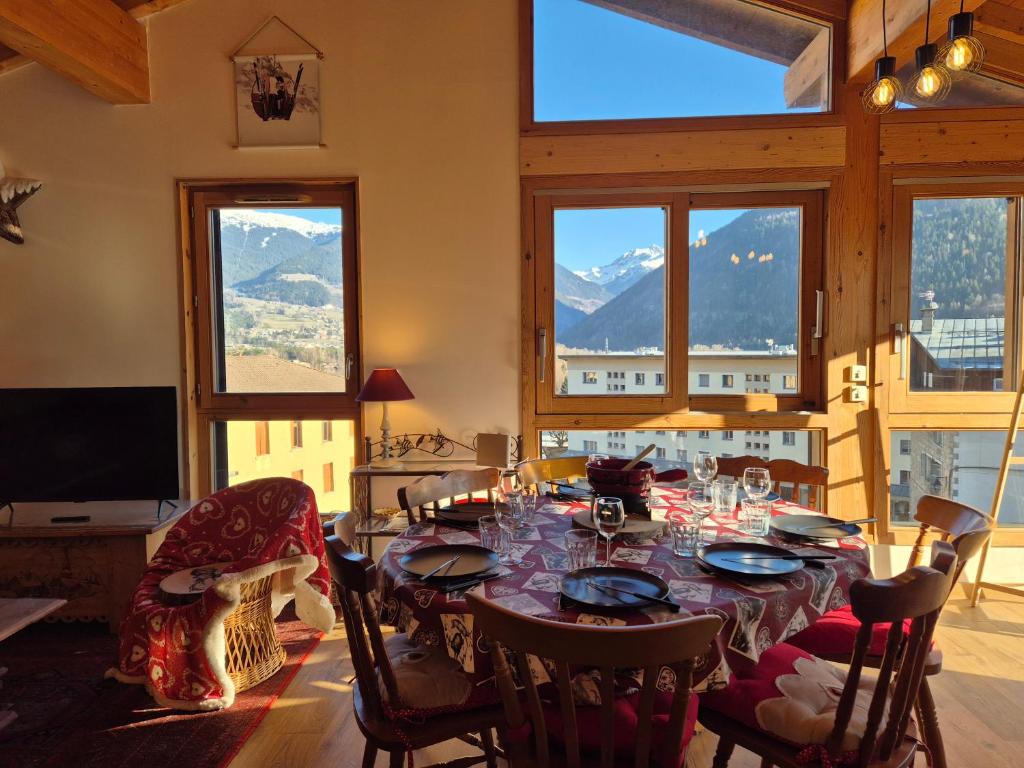 a dining room with a table and chairs and windows at Sublime appartement avec terrasse - Centre BSM in Bourg-Saint-Maurice