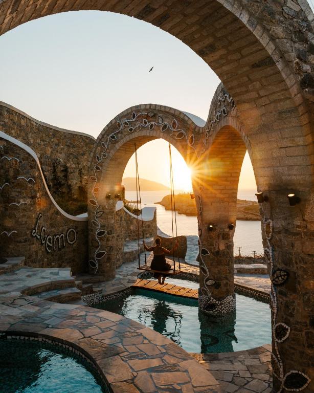 a woman sitting on a swing in a pool with the sunset at Agalia Luxury Suites in Tzamaria