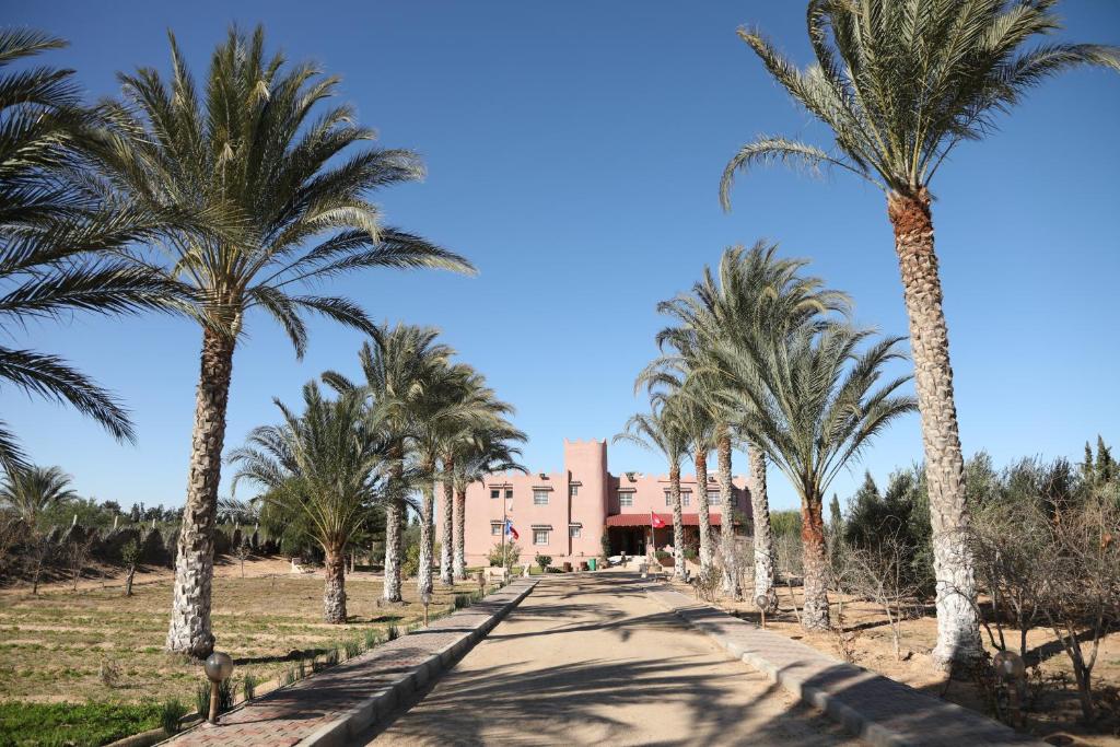a road lined with palm trees in front of a building at Dar Elferdaous in Al Medou
