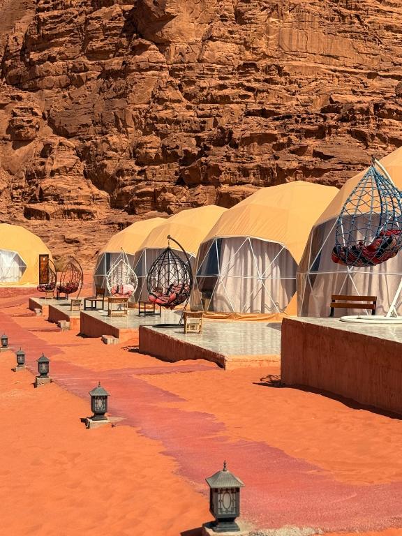 a row of tents in a desert with a rock wall at NAEL BEDOUIN Camp in Wadi Rum