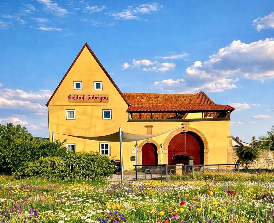 a yellow building with a red roof and a field of flowers at Landhaus Sofie in Kreischa