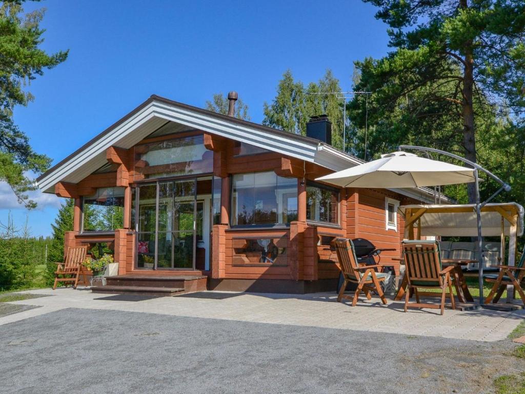 a wooden cabin with chairs and an umbrella at Holiday Home Kannelpirtti 1 by Interhome in Puromäki