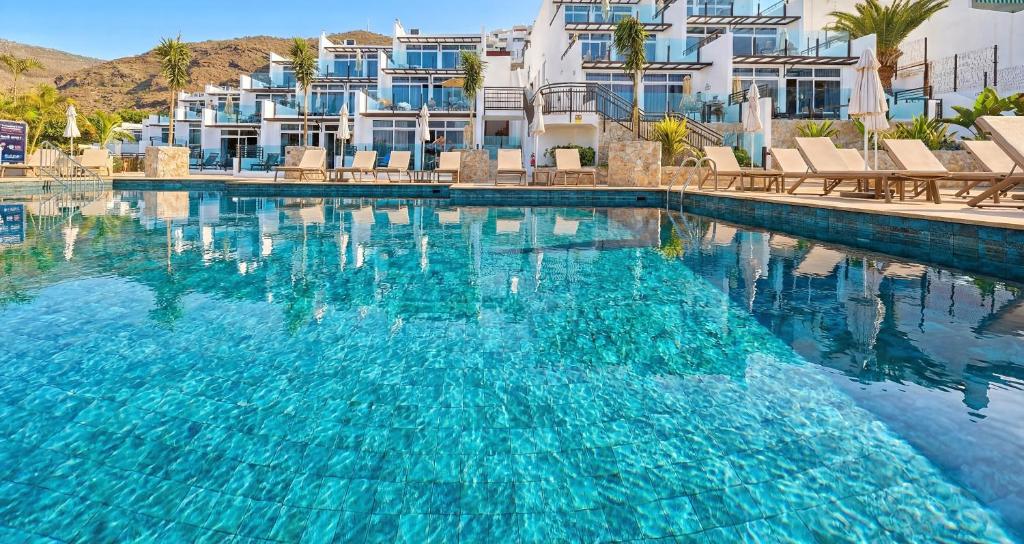 a swimming pool with blue water in front of buildings at Sunset Suites by Bull Hotels in Puerto Rico de Gran Canaria