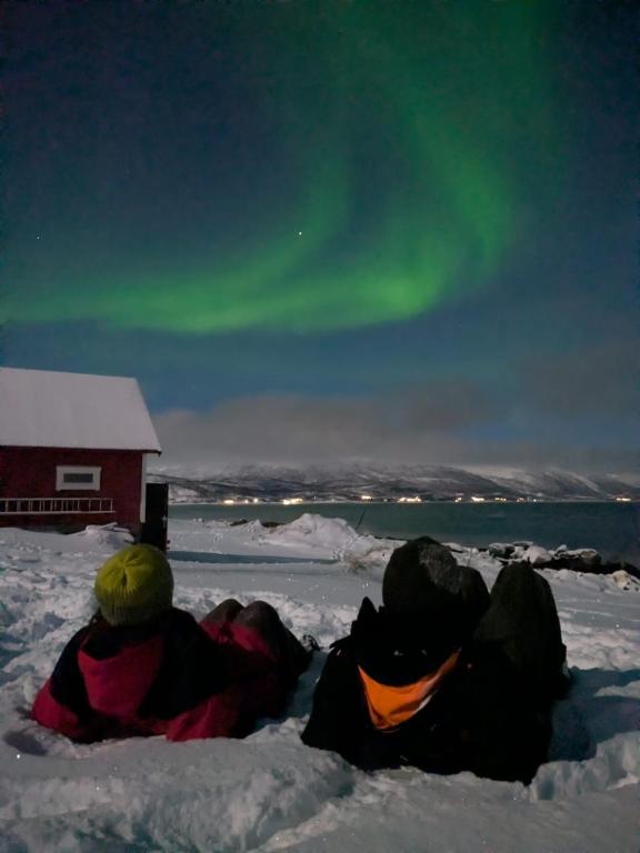 a group of people laying in the snow in front of a barn at Idyllic familyhouse by the sea with ponorama view in Tromsø