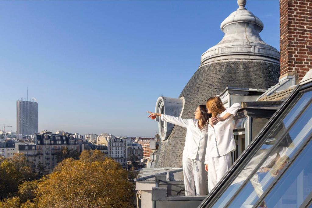 two women in white suits standing on the ledge of a building at Hôtel de Banville in Paris