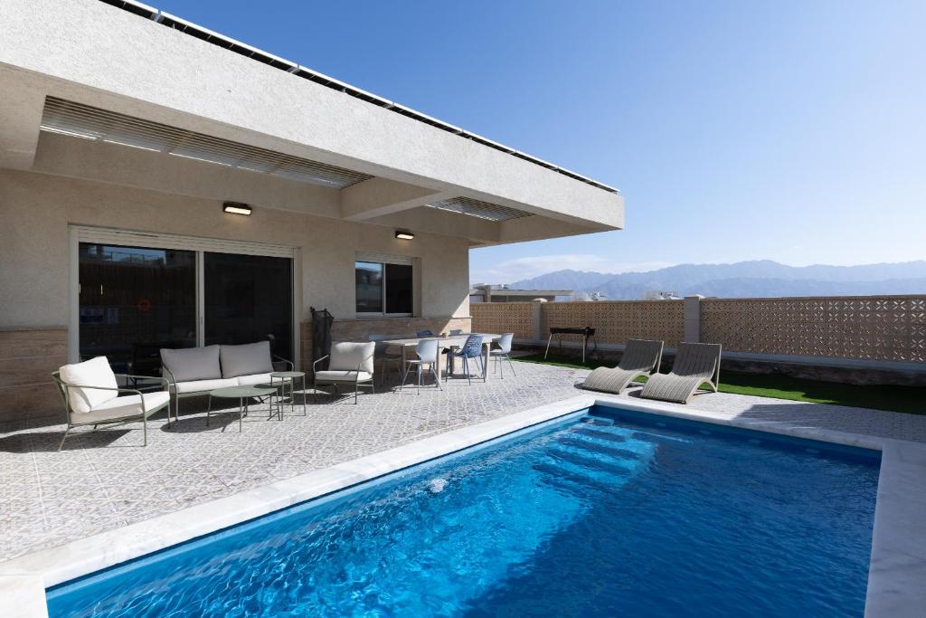 a backyard with a swimming pool and chairs and a house at וילה פאן 4 חדרי שינה בריכה מחוממת Villa Fun 4 BR Heated Pool in Eilat