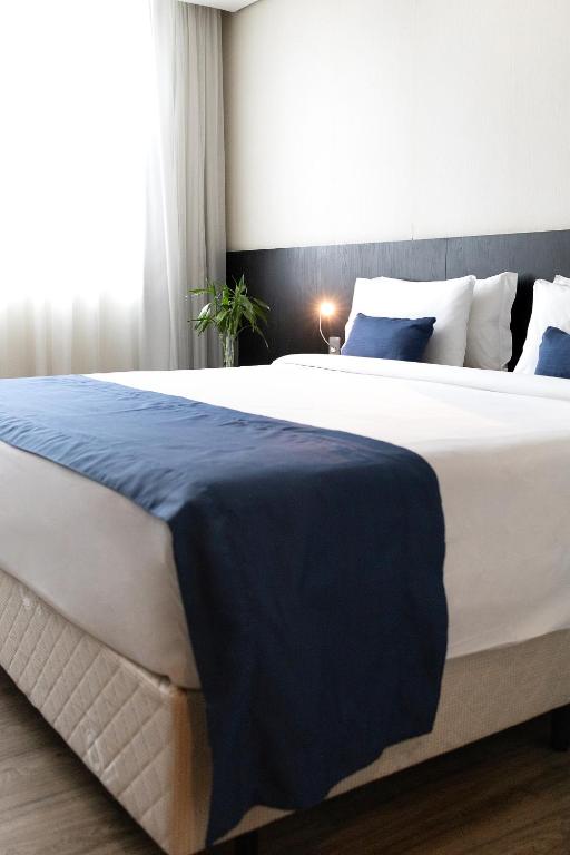 a large bed with a blue blanket on it at Hotel Park Tower Savassi by Nacional Inn in Belo Horizonte