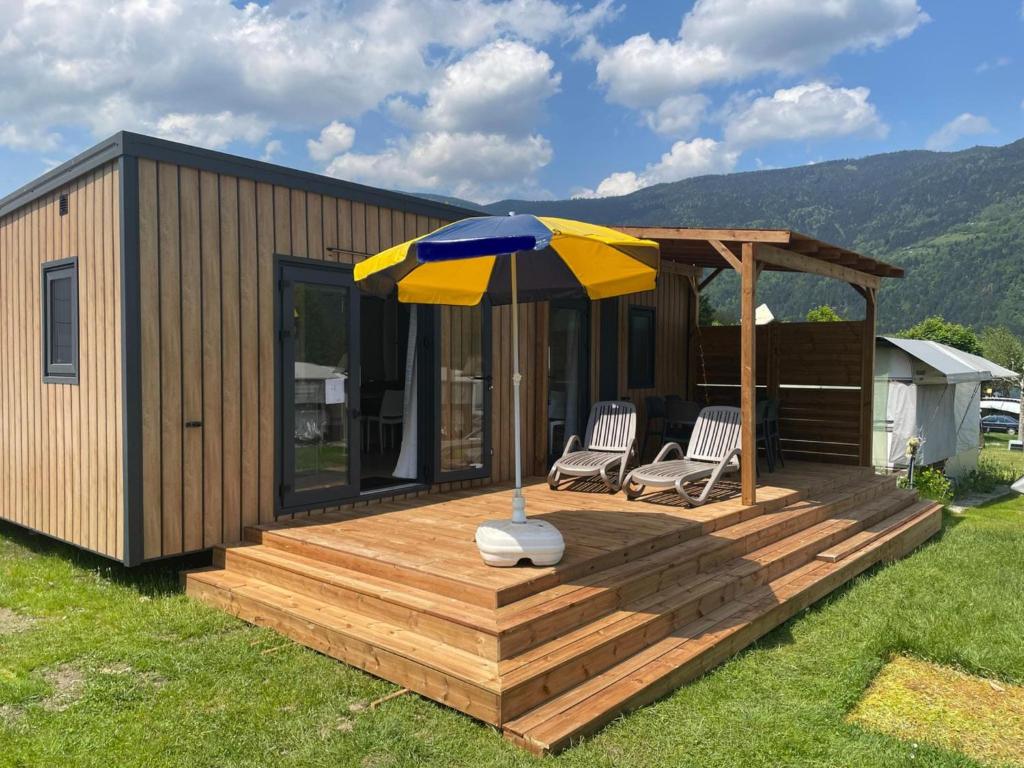 a house with an umbrella and two chairs on a deck at Mobile Home in Austrian Countryside in Altossiach