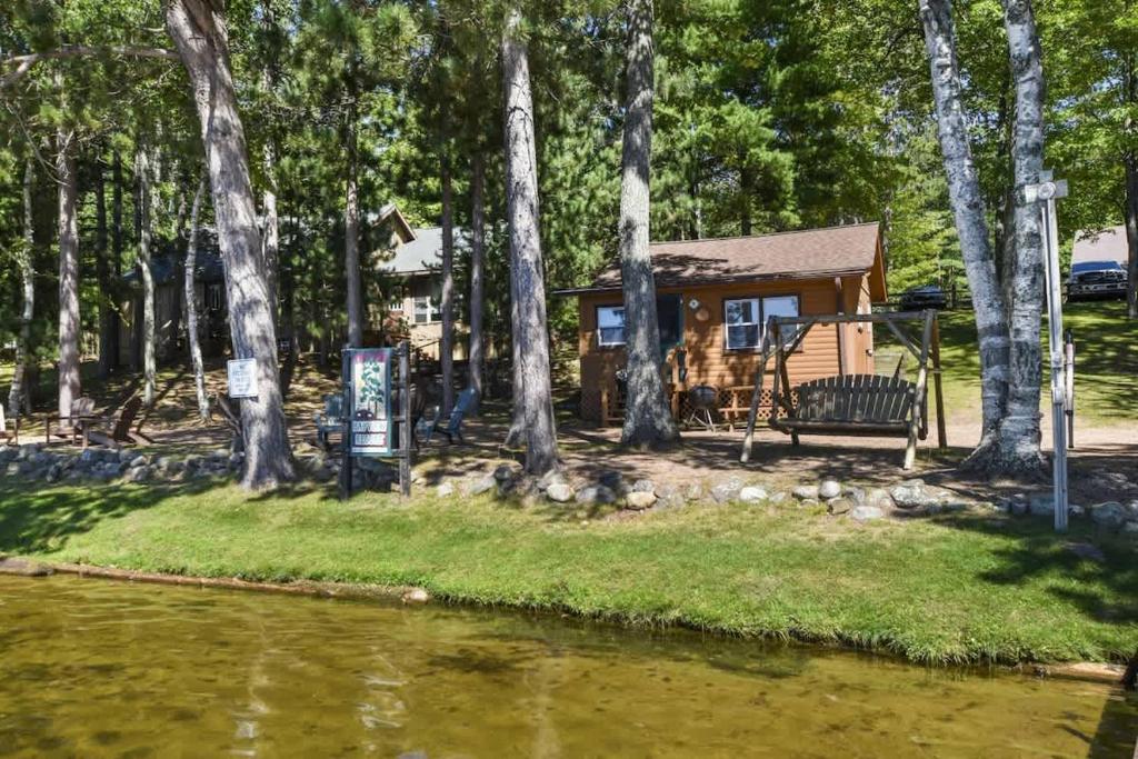a cabin by a river with a bench and trees at Bayview Resort Sandy Shores Cabin 3 in Saint Germain