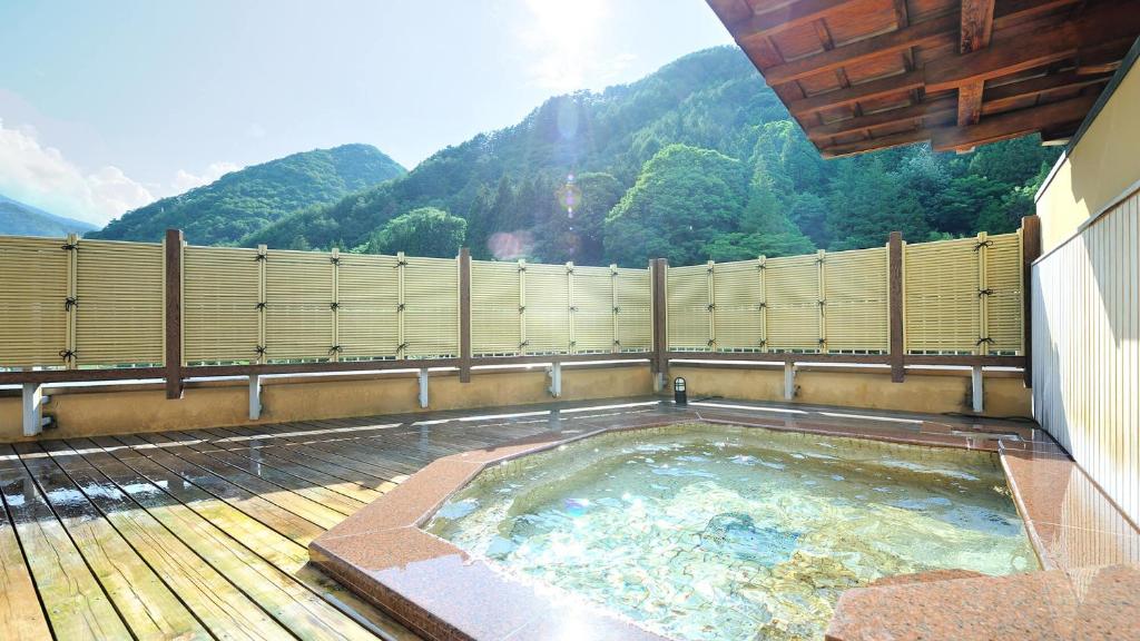 a hot tub on a deck with mountains in the background at Bouzantei Kotobuki in Ueda