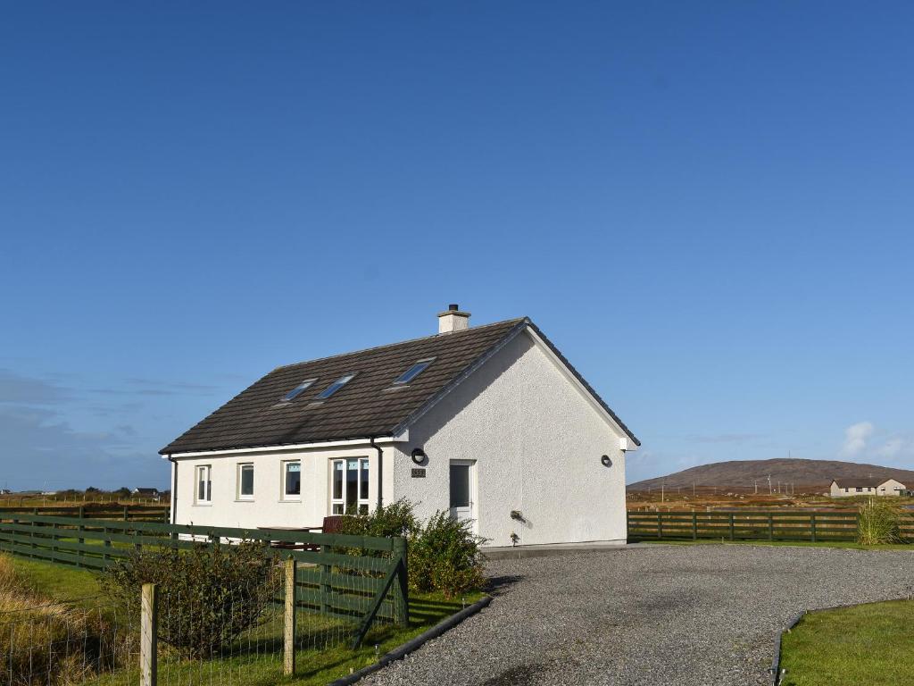 a white house with a black roof on a road at Lochboisdale Cottage in Lochboisdale