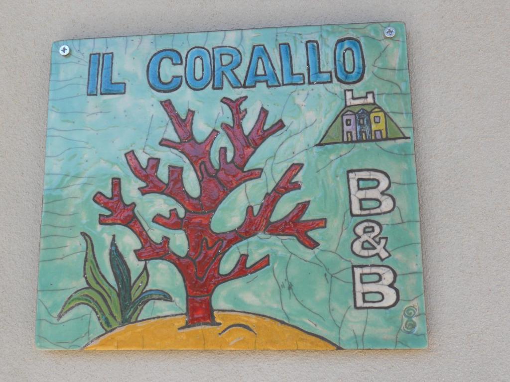 a sign on a wall with a tree and a house at B&B Il Corallo in Bosa