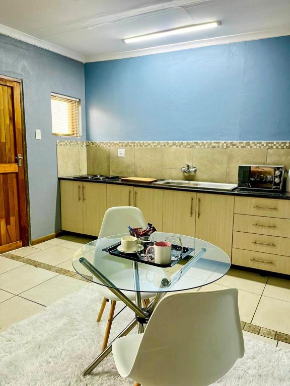 a kitchen with a glass table and white chairs at Palmetto guesthouse in Mahikeng