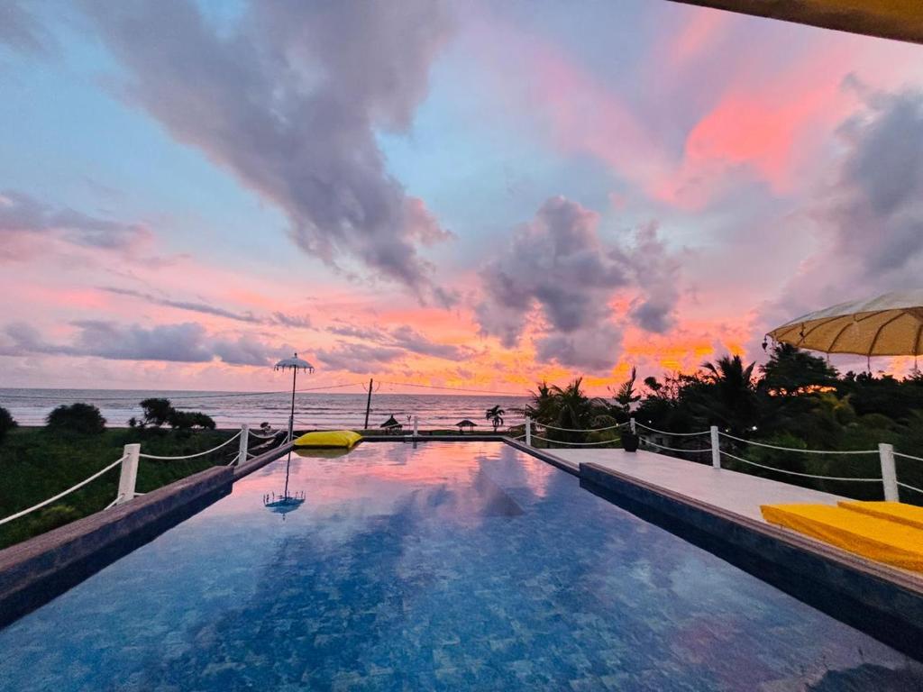 a swimming pool with a sunset in the background at Trika Surfcamp Bali in Airsatang