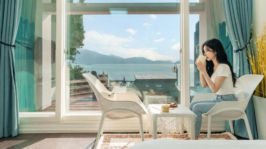 a woman sitting on a porch drinking a cup of coffee at Namhae Opera House Pension in Namhae