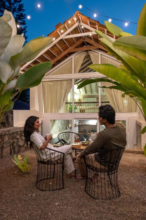 two people sitting at a table in front of a building at Tool House - Great Estate Stay for Remote Work in Siddapur