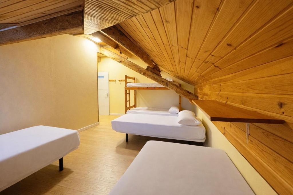 a room with two beds and a wooden ceiling at Albergue Pájaro L in Castejón de Sos