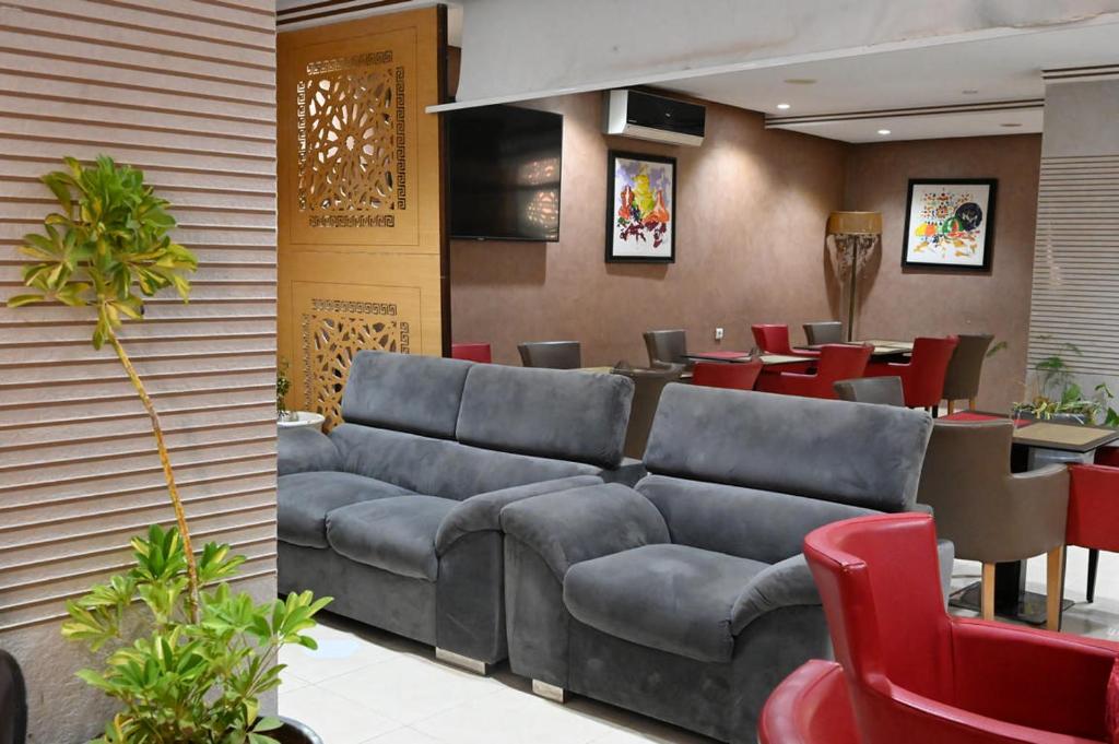 a waiting room with a large couch and red chairs at Hôtel Vallée Ziz in Er Rachidia