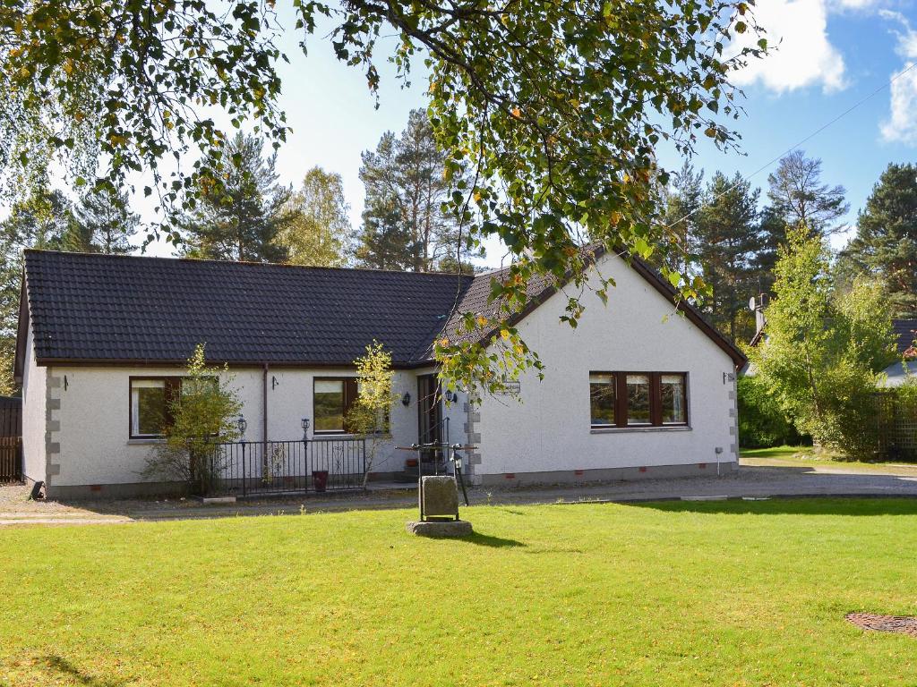 a white house with a black roof on a yard at Cotterton Beag in Nethy Bridge