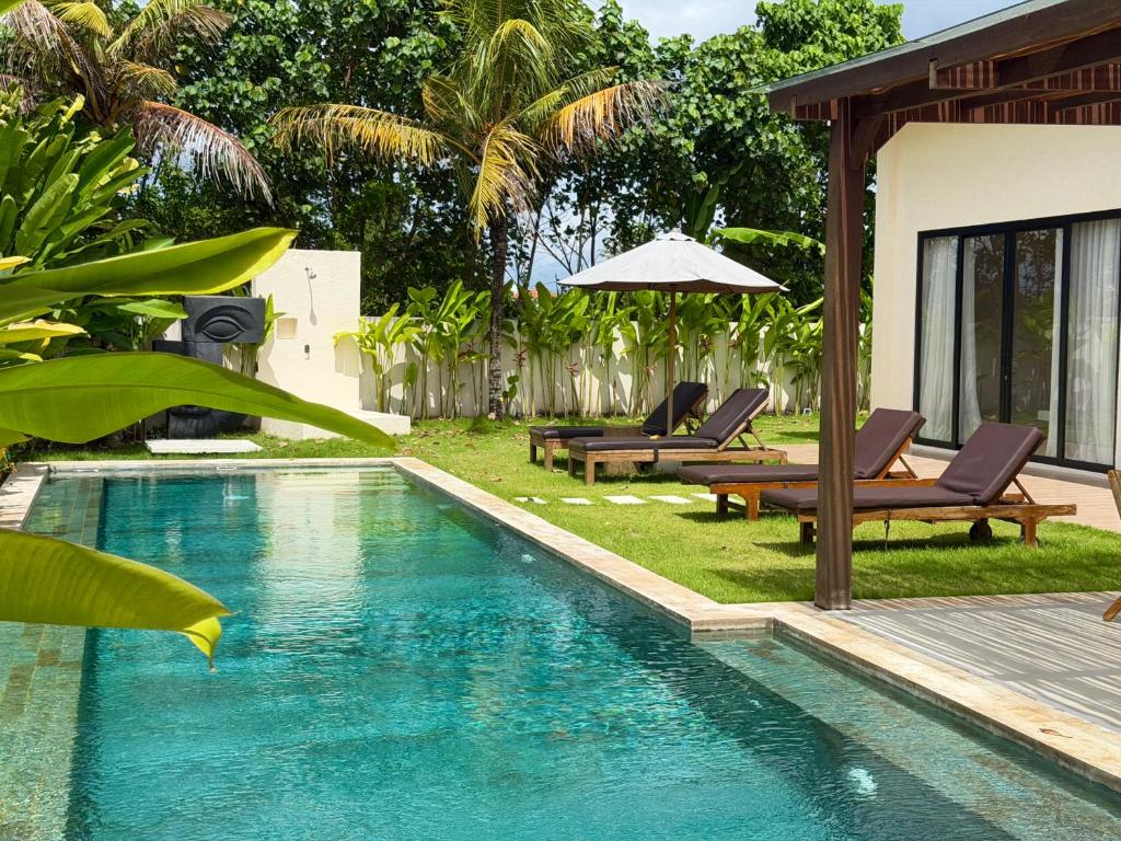 a swimming pool in a backyard with chairs and an umbrella at Villa YAOUH à Seseh in Munggu