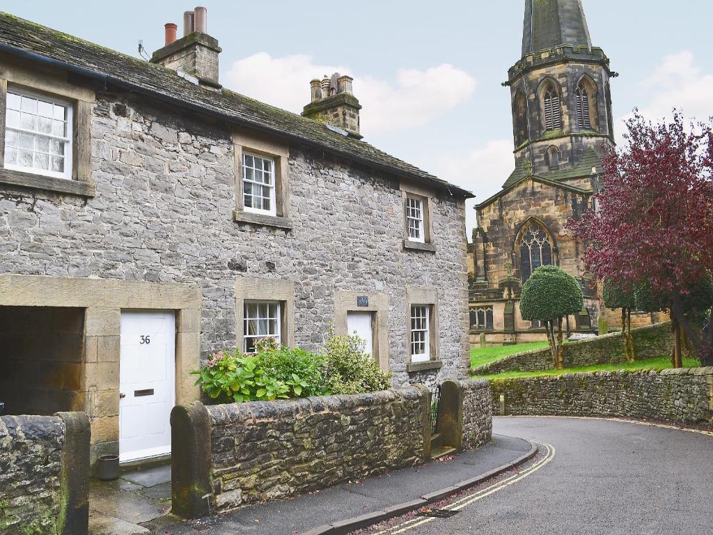an old stone building with a church in the background at Corner Cottage in Bakewell