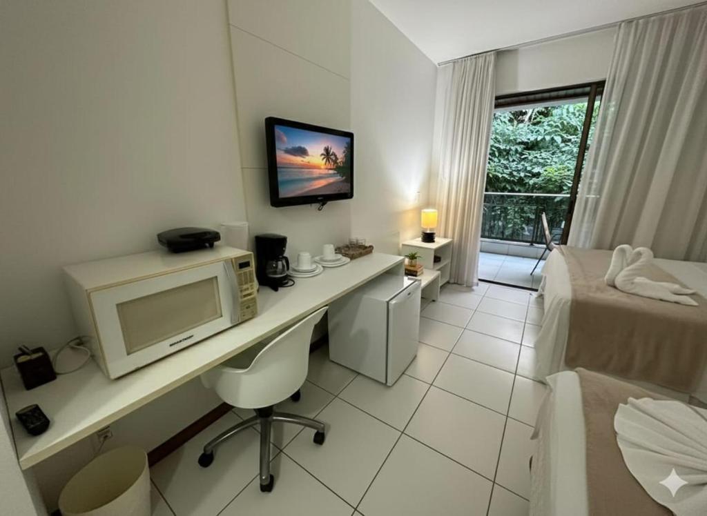a hotel room with a desk with a television and a bed at Iloa Studio Alagoas conforto e encantamento in Barra de São Miguel