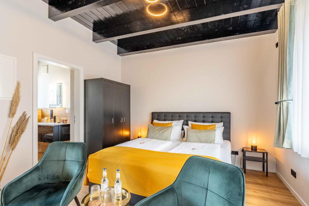 a bedroom with a bed and two green chairs at LÜTTES LOFT Boutique Hotel in Eckernförde
