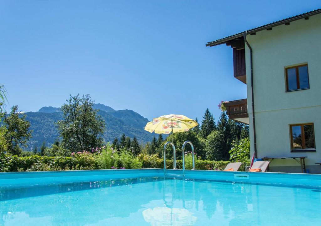 a swimming pool with an umbrella next to a house at Ferienhaus Waldhof in Hermagor