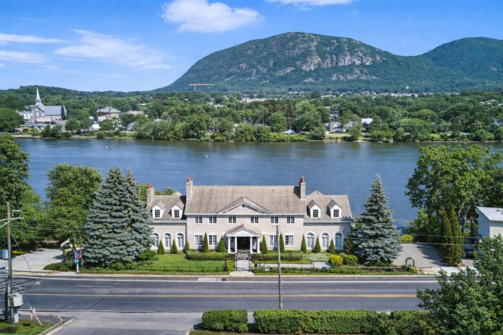 a large house on the river with mountains in the background at Waterfront Mansion with Mont-Saint-Hilaire Views, Near Montreal in Beloeil Village