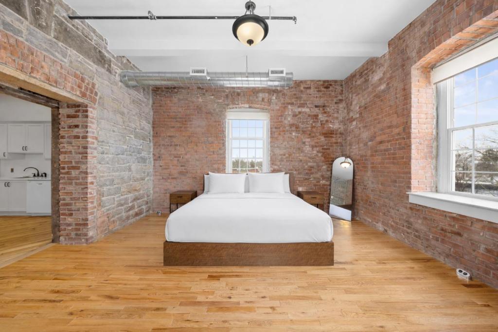 a brick walled bedroom with a bed with white sheets at Tri Century Mill Suites in Carleton Place