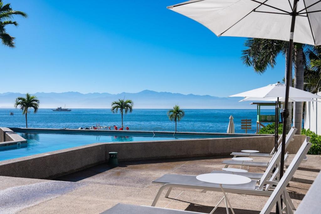 a pool with chairs and an umbrella and the ocean at Zantamar 105B, a pie de playa in Cruz de Huanacaxtle