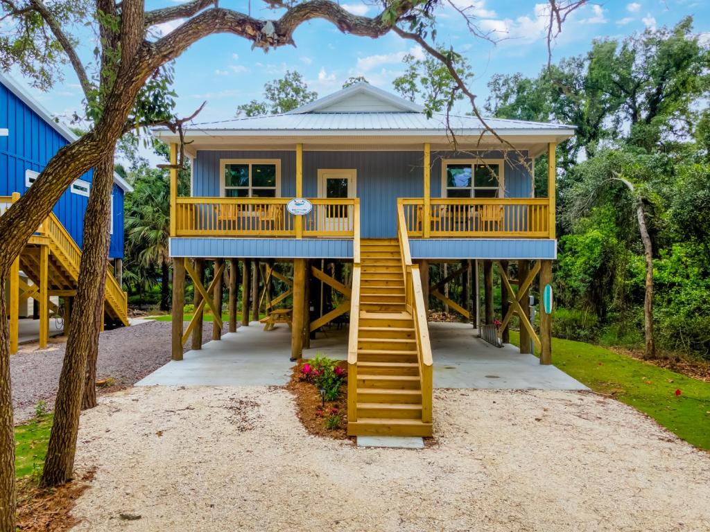 a house with blue and yellow stairs and trees at Lavender Haze - 1209 Chaumont in Dauphin Island
