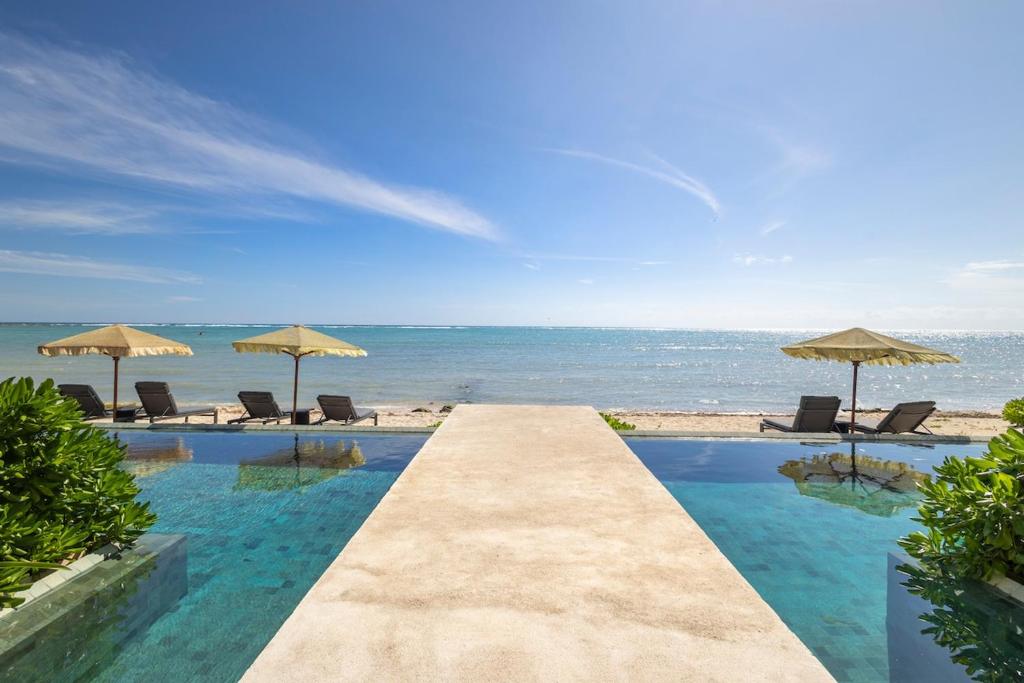 a swimming pool with chairs and umbrellas on the beach at Beachfront 2BR Condo in Bahía Tankah, Tulum in Tancah
