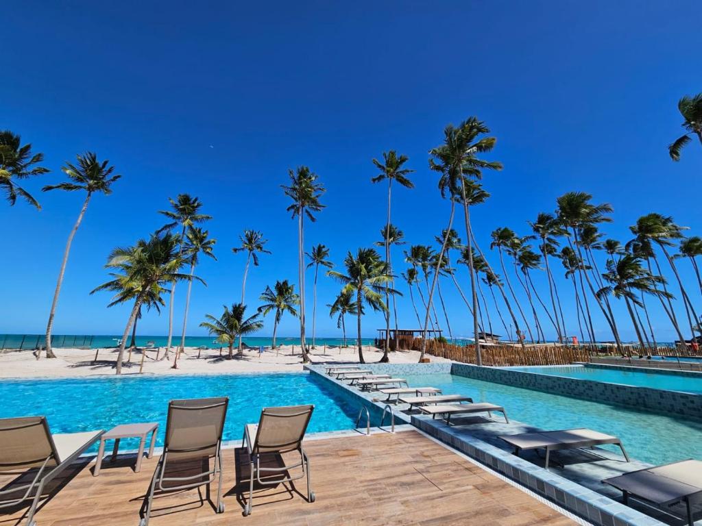 a pool with chairs and palm trees on the beach at Apartamento Ipioca Beach Life in Ipioca