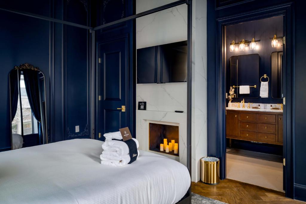 Navy-walled bedroom with four-poster bed, wall-mounted TV, marble fireplace, and en-suite bathroom with brass fixtures at The Highliner Hotel in Gloucester