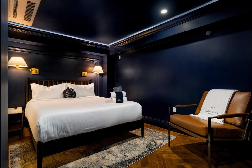 King bed with white linens, brass wall sconces, navy paneled wall, bench with folded towels and Highliner Hotel branded chair at The Highliner Hotel in Gloucester