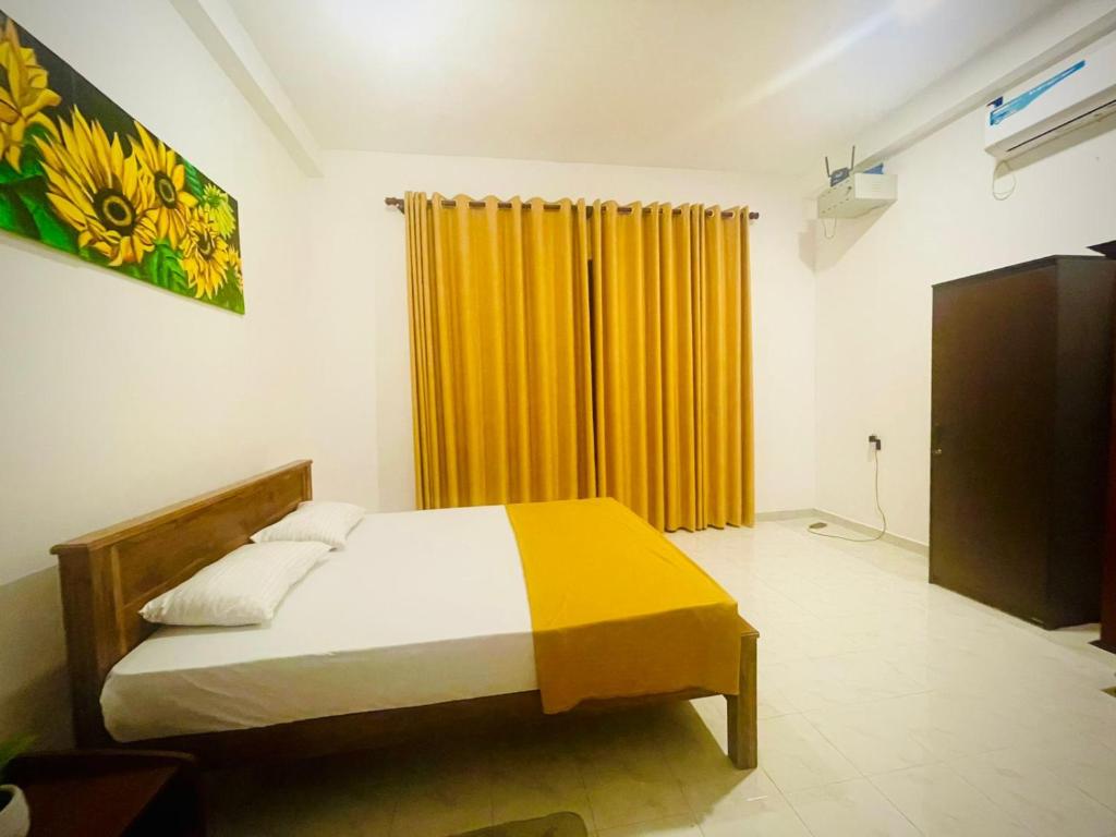 a bedroom with a bed and a yellow curtain at Delmar Homestay in Dickwella