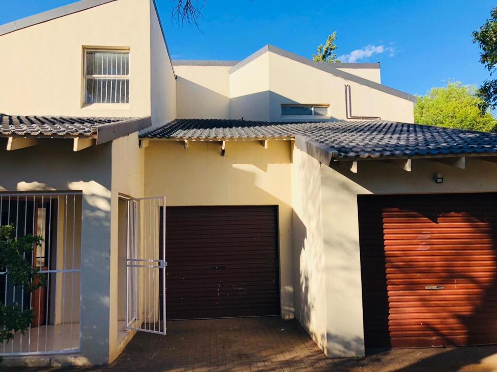 a white house with a garage and a building at Twin Power Guesthouse in Bloemfontein