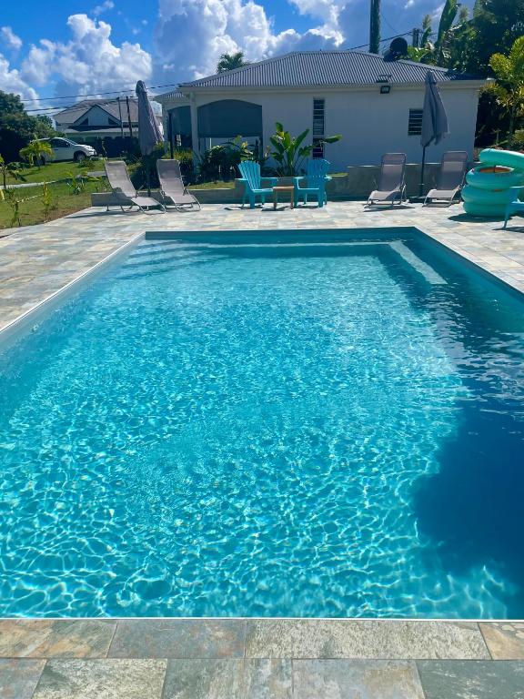 a blue swimming pool with chairs and a house at Mango-passion Le Domaine Mannou in Sainte-Rose