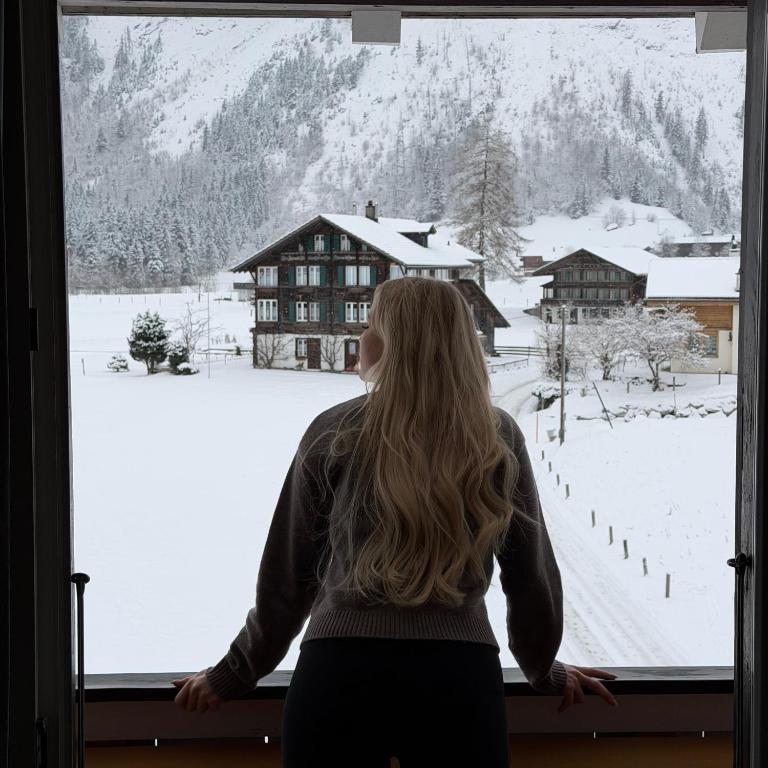 Eine Frau blickt aus dem Fenster auf einen schneebedeckten Berg in der Unterkunft Waterfall View in Kandersteg