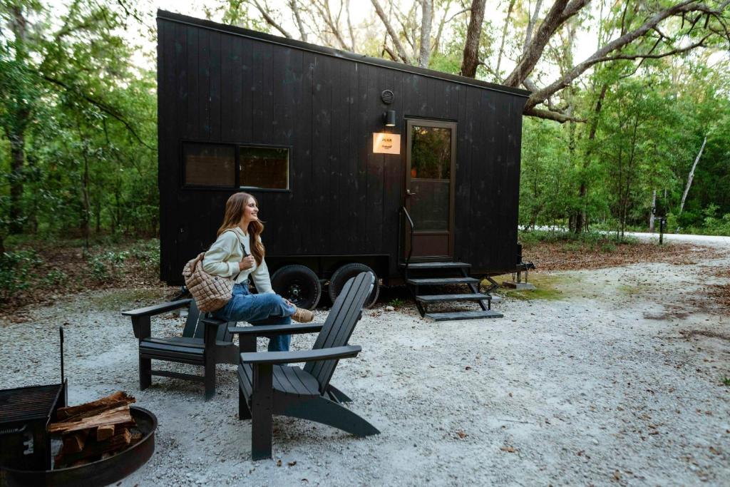 a woman sitting on a bench in front of a black tiny house at Postcard Cabins Shenandoah, Outdoor Collection by Marriott Bonvoy in Stanardsville