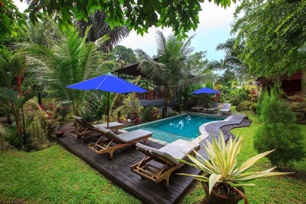 a swimming pool with chairs and umbrellas next to a yard at Bali Sesandan Garden in Tabanan